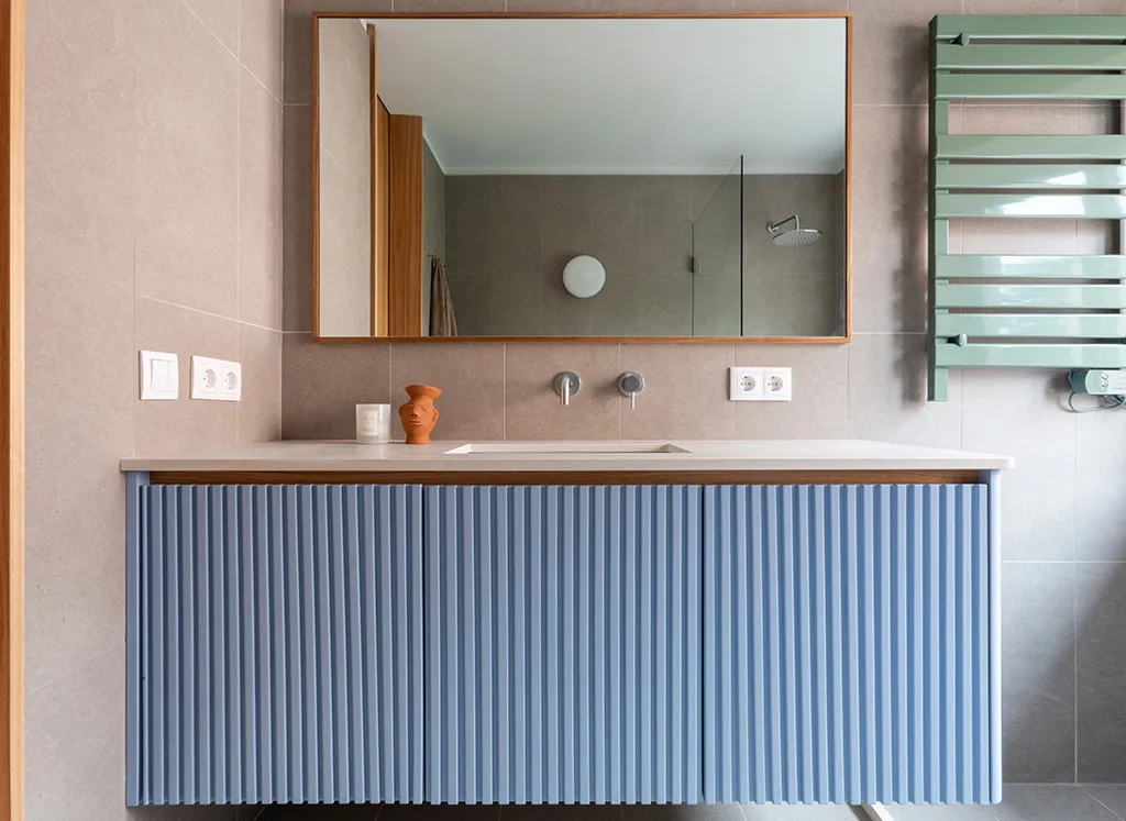 A bathroom with a fluted blue vanity and a stone-toned wall, by Rita Bessa Arquitectura