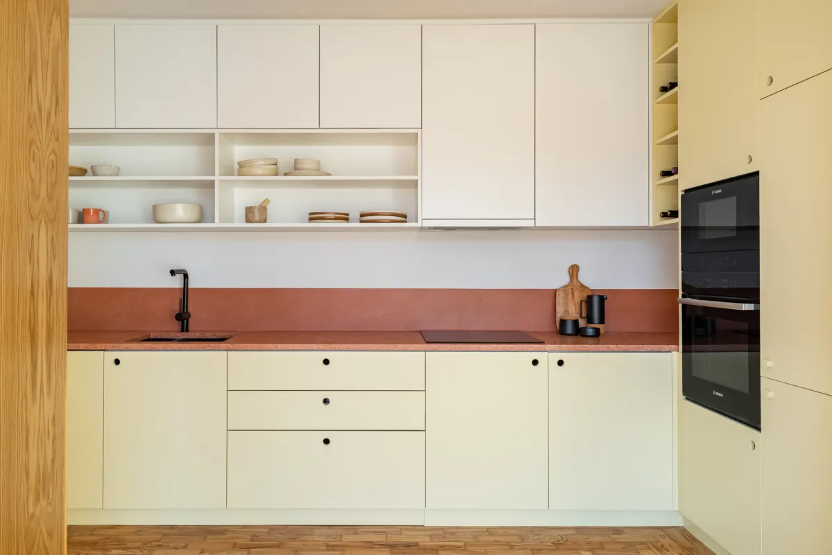 A kitchen in pale yellow joinery with a terracotta worktop and open shelving, by Santo Infante