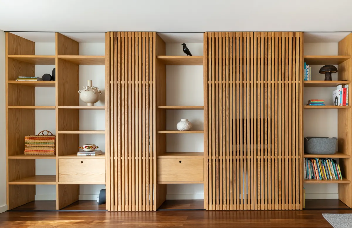 A wall of oak shelving with slatted sliding panels, by Santo Infante