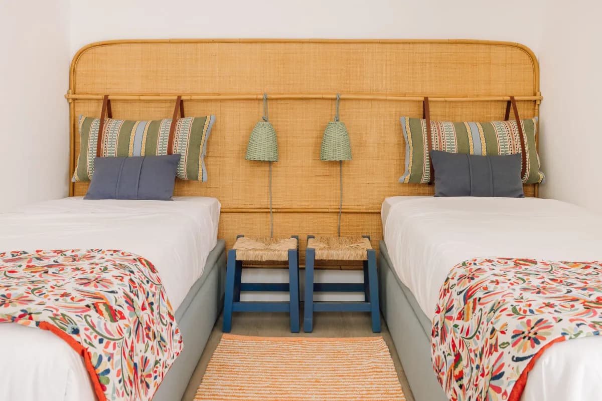 Twin beds under a rattan headboard with woven pendant lamps and embroidered throws, by Santo Infante